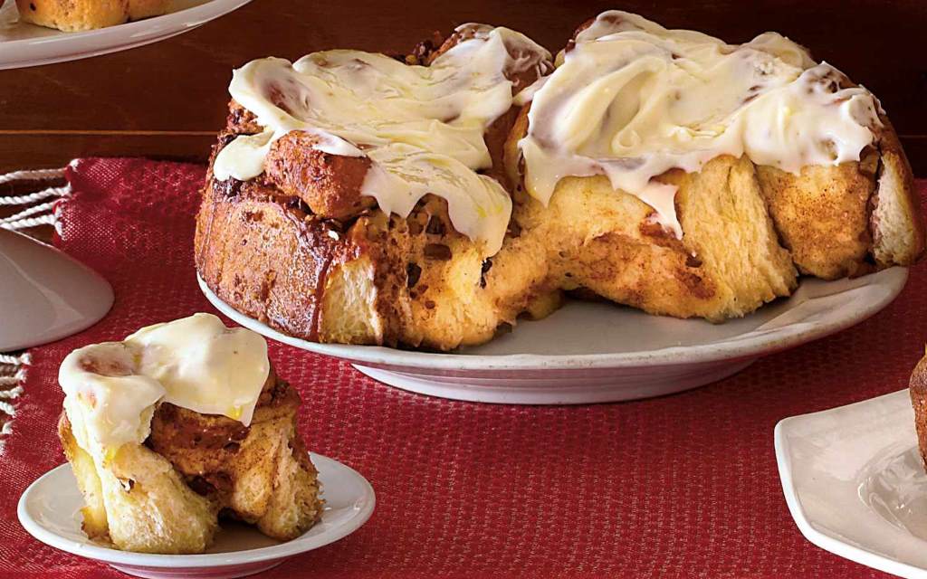 Warm cinnamon rolls topped with creamy, glossy cream cheese icing on a white plate