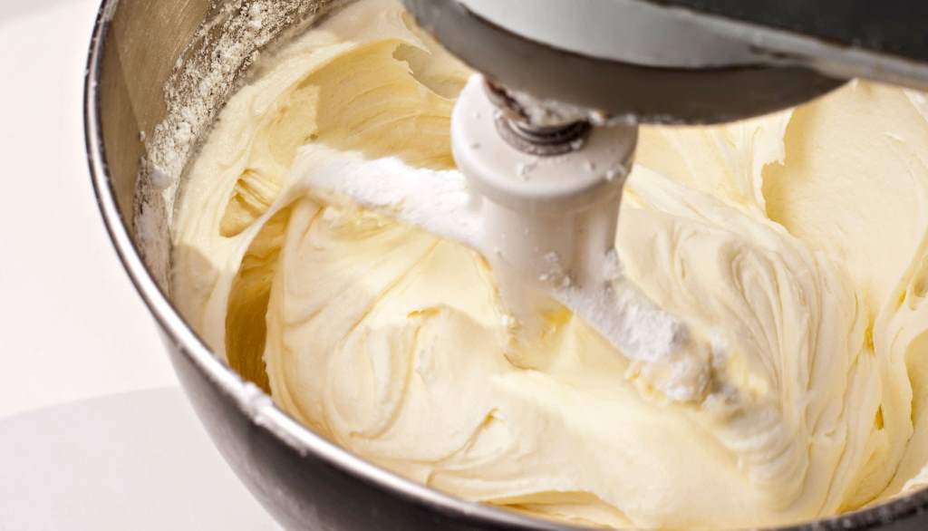 Stand mixer with whisk attachment blending smooth cream cheese icing in a stainless steel bowl